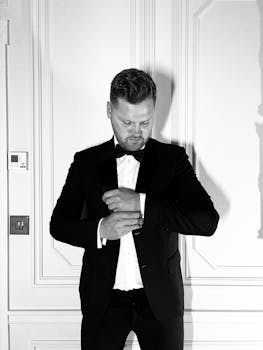 Stylish man in a tuxedo adjusting his cufflinks, exuding elegance in a London setting.