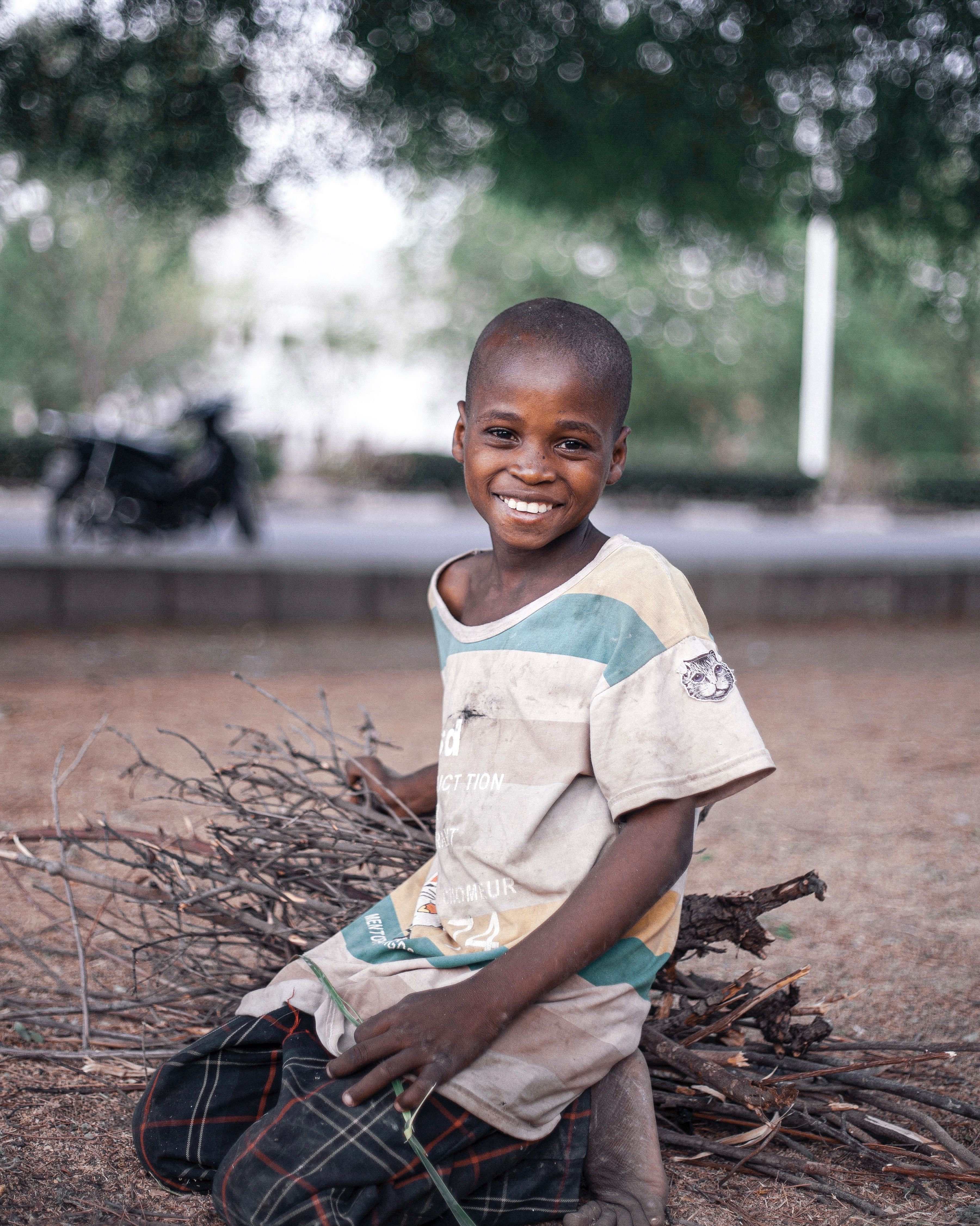 Young African boy smiling while gathering sticks outdoors, showcasing joy and resourcefulness.