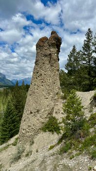 Hoodoo rock formation amidst a lush forest and mountainous backdrop under a bright sky.