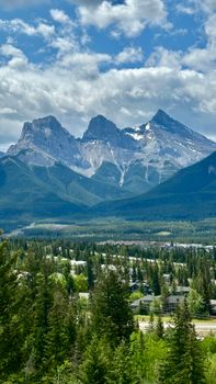 Breathtaking summer view of Three Sisters Mountain and forested landscape under a cloudy sky.