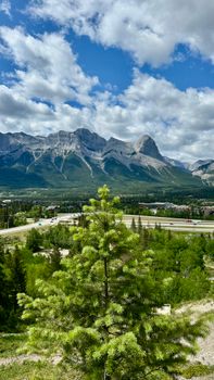 Breathtaking landscape of the Canadian Rockies with lush greenery and blue cloudy skies in the background.