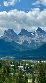 Scenic landscape of the Three Sisters peaks in the Rocky Mountains under a cloudy sky.