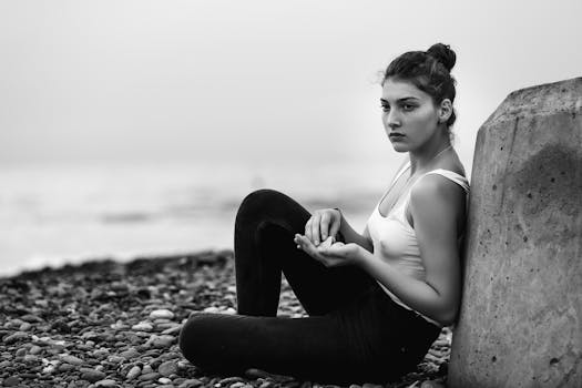 Black and white portrait of a woman sitting on a rocky beach, exuding contemplative elegance.