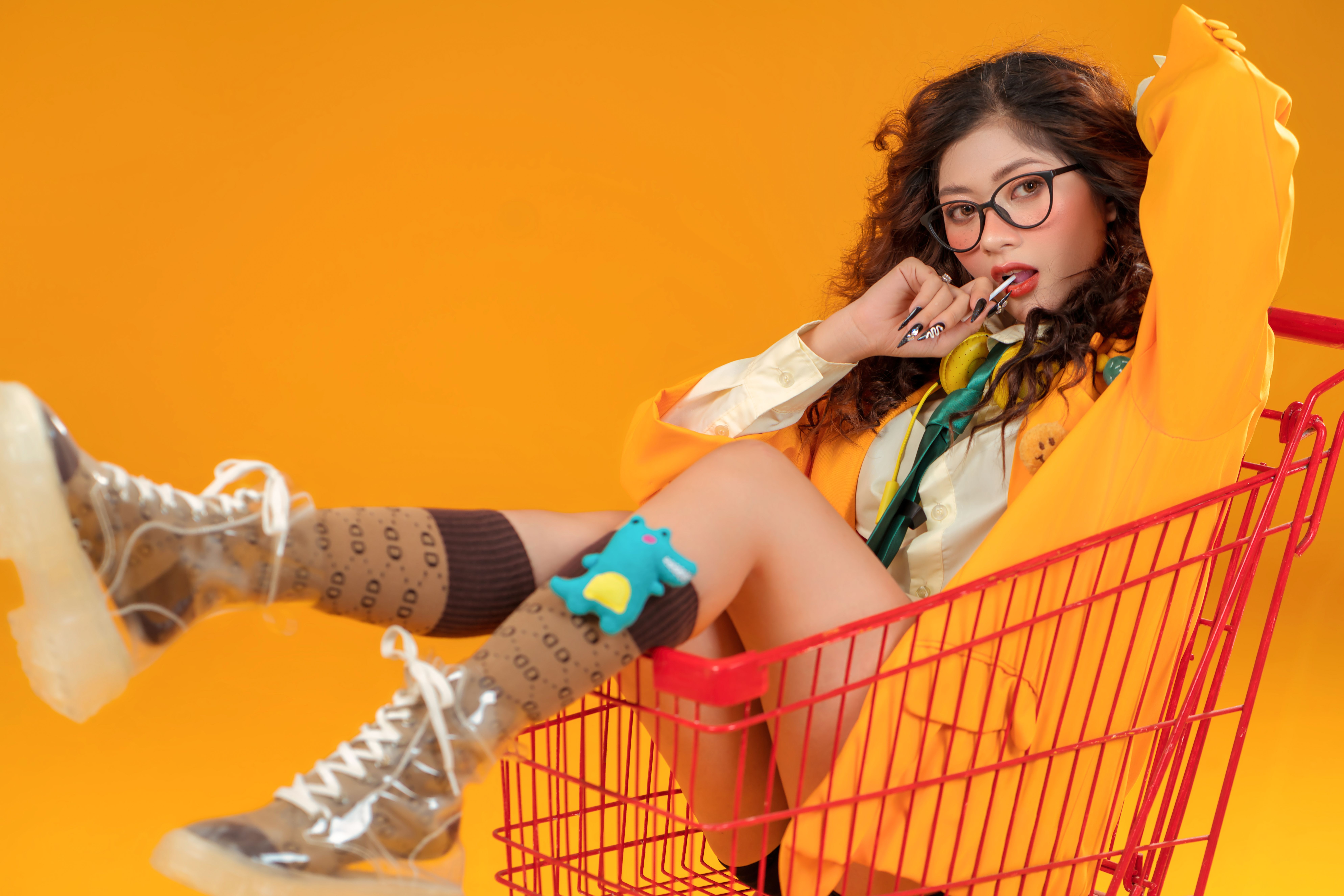 Stylish young woman in a shopping cart, vibrant orange background.