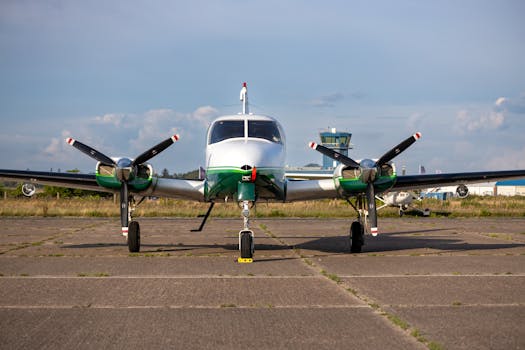 A twin-engine airplane parked on a sunny tarmac with a control tower in the background.