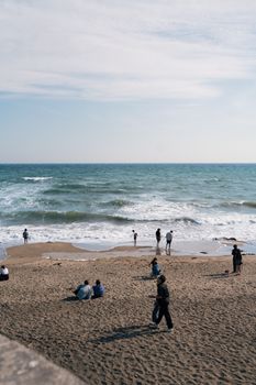 People enjoying a sunny day on Kamakura Beach, Japan with blue skies and gentle waves.