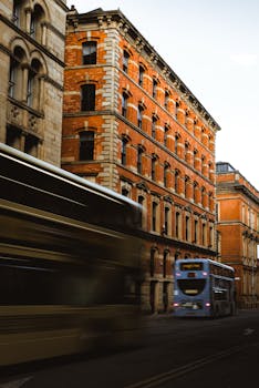 Blurred motion of buses passing by a historic brick building on a city street.