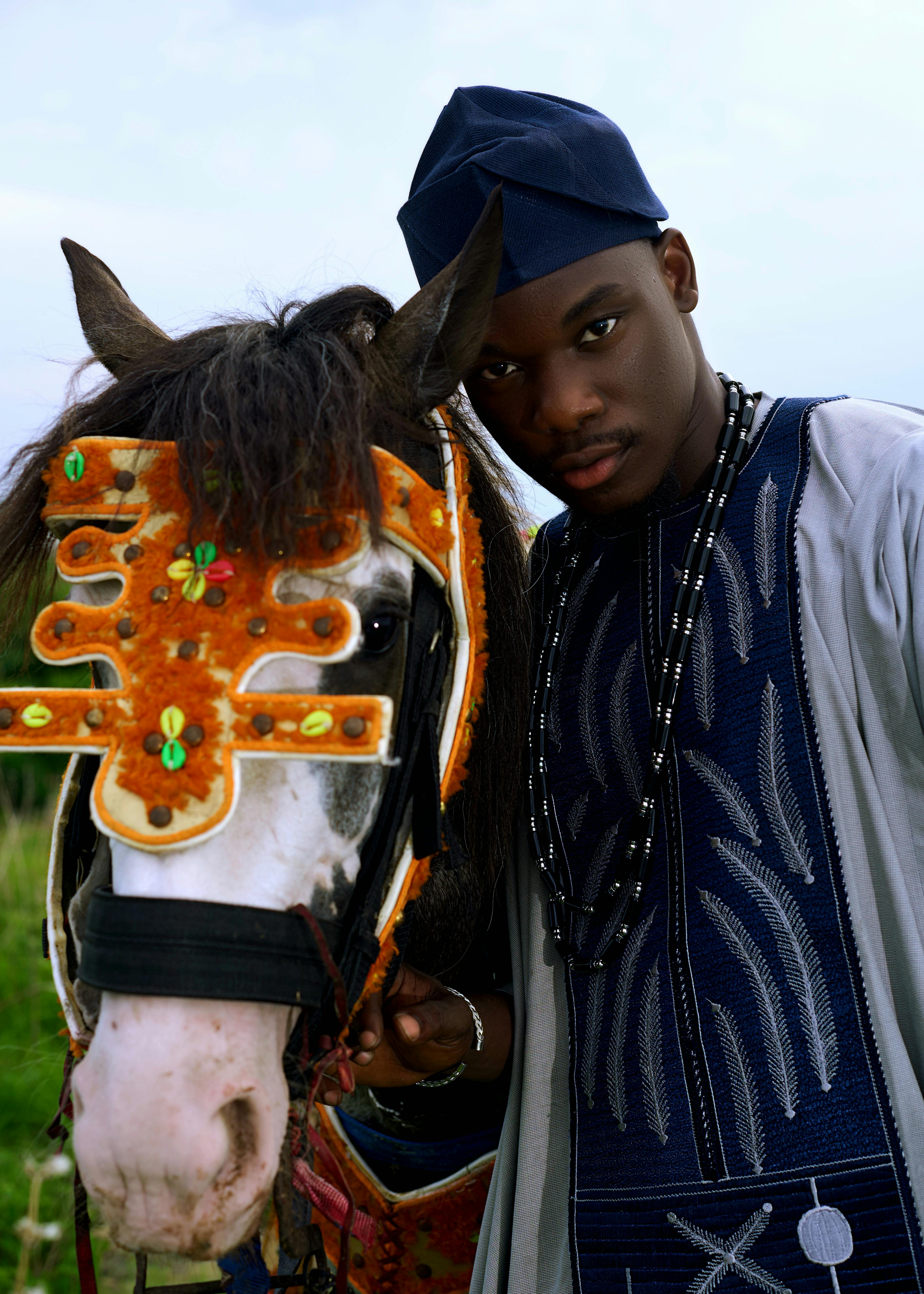 Man in traditional attire alongside a beautifully adorned horse in an outdoor setting.