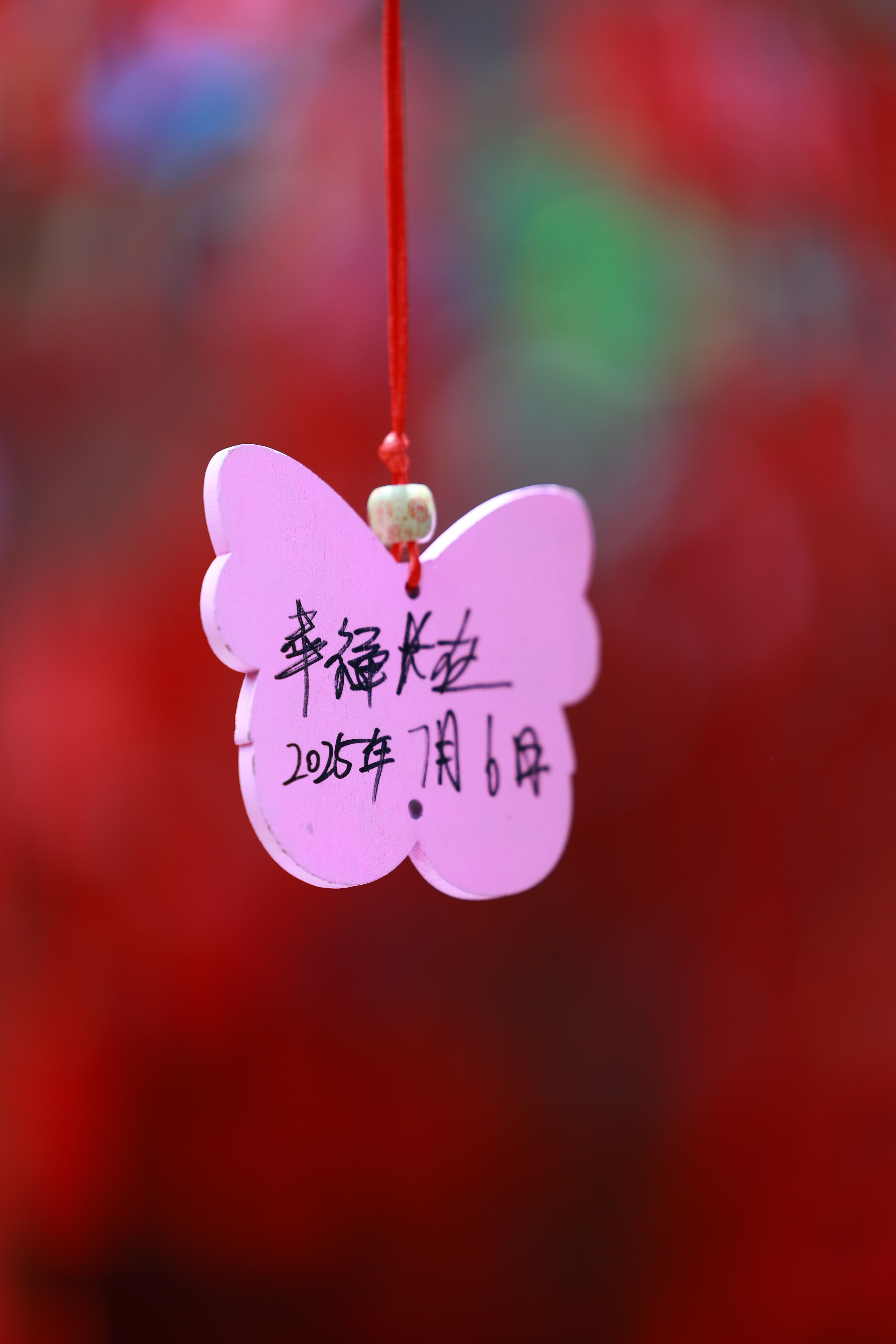 A pink butterfly charm with handwritten text, symbolizing wishes or blessings.