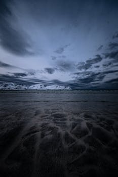 A captivating view of a beach with snowy mountains and dramatic clouds at twilight.
