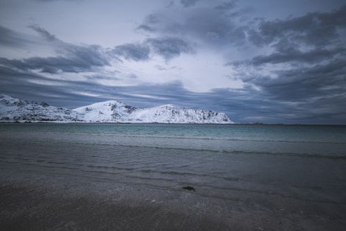 Free Dramatic winter coastal scene with snowy mountains and moody clouds over the sea. Stock Photo