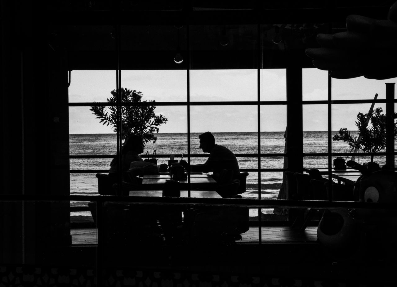 silhouetted diners enjoy a meal by the ocean framed by large windows a