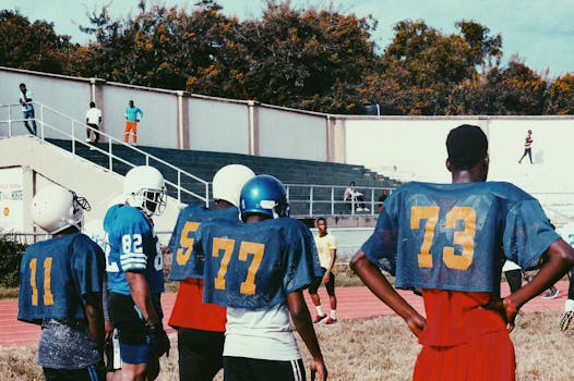 Young men in football gear prepare for practice on an outdoor field.