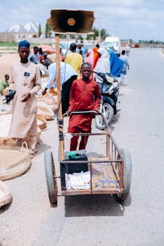 Young vendor with cart selling goods at a lively outdoor market.
