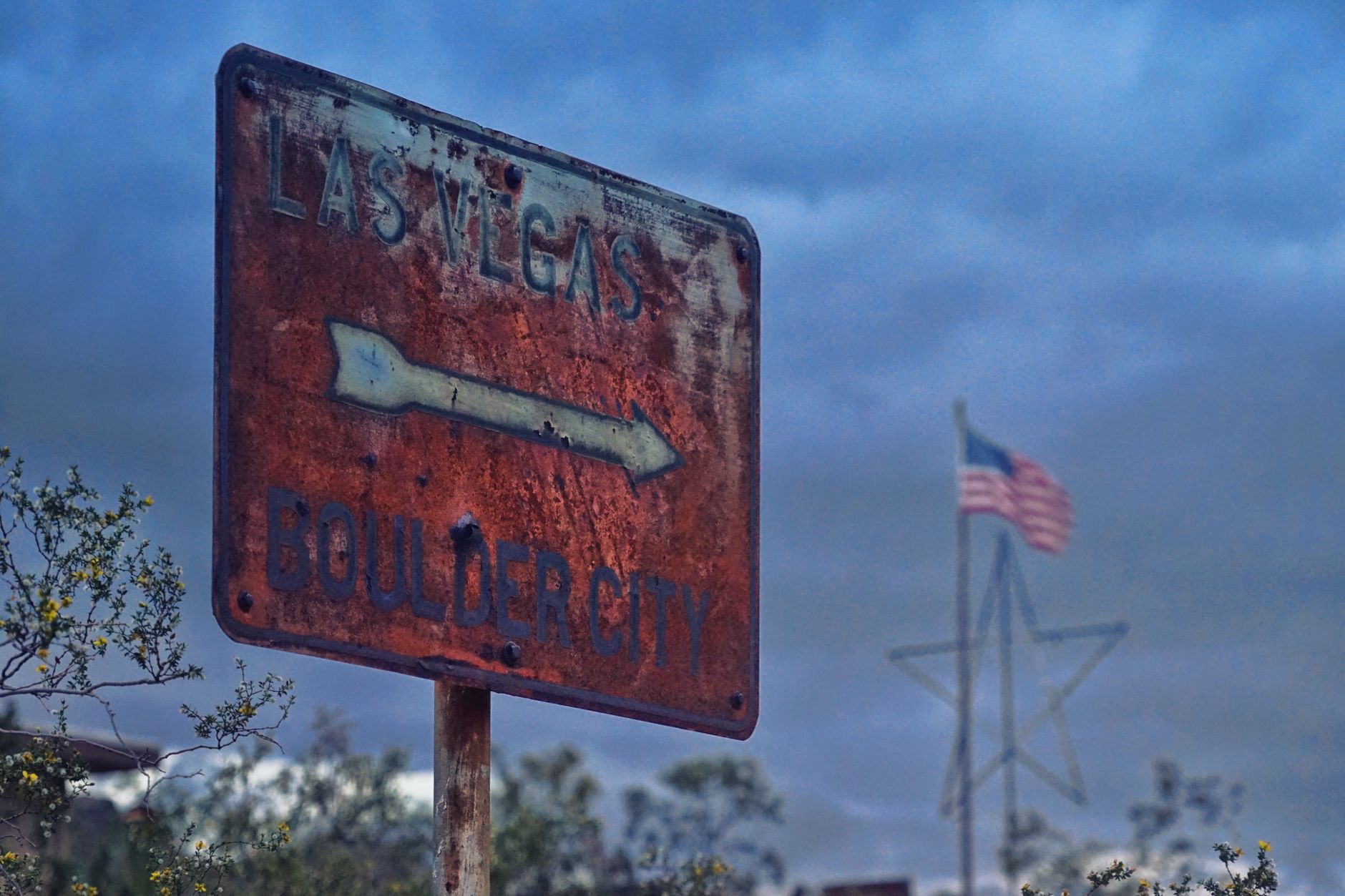Vintage road sign pointing to Las Vegas and Boulder City against a blue sky.