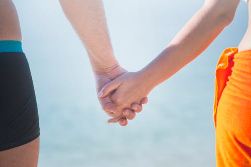 Au Milieu Du Couple Se Tenant La Main à La Plage Contre Le Ciel