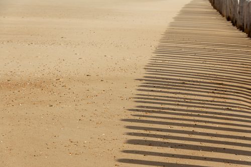 Free Minimalistic sandy beach scene with wooden piling shadows creating a striking pattern. Stock Photo