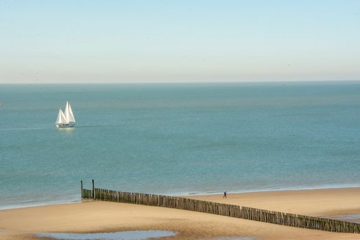 A peaceful sailing ship on calm waters with a sandy beach and clear sky.