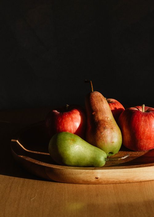 Free Ripe whole green pears and red apples placed on wooden board on table in dark room illuminating by sunny rays Stock Photo