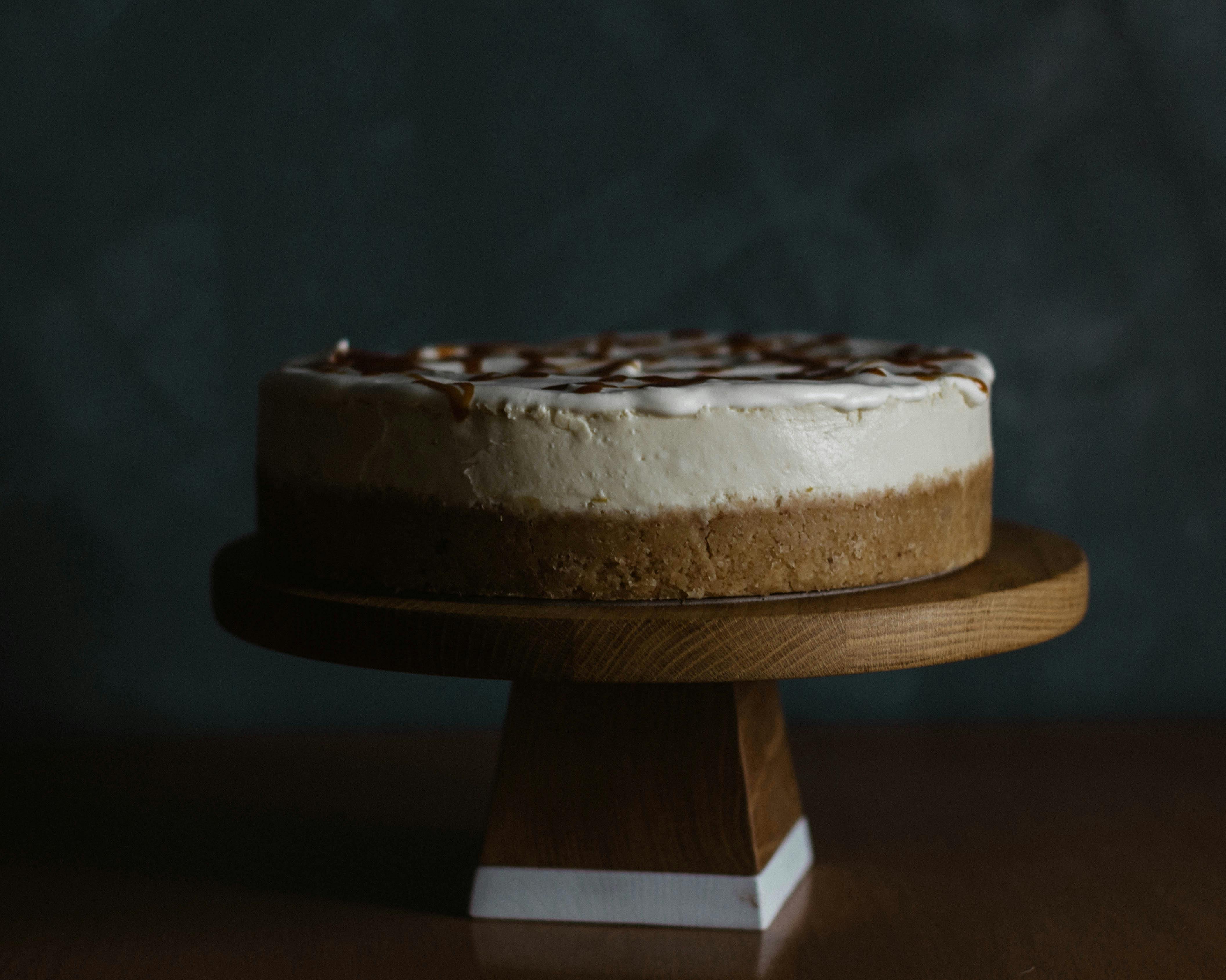 Delicious homemade cheesecake made from different kinds of chocolate garnished with topping and served on wooden pedestal cake plate on table against dark blue wall