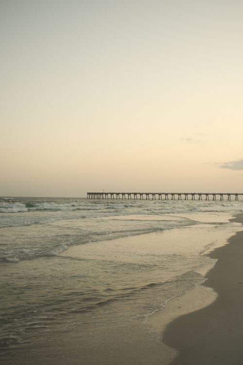 Free Peaceful beach scene at sunset with a pier extending into the ocean. Stock Photo