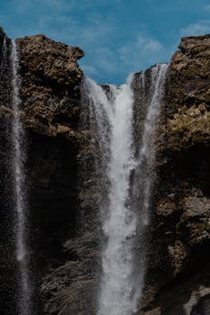 A stunning waterfall cascades between rocky cliffs against a bright blue sky.