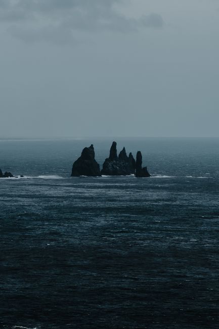 Moody ocean view featuring the iconic Reynisdrangar sea stacks under a cloudy sky.