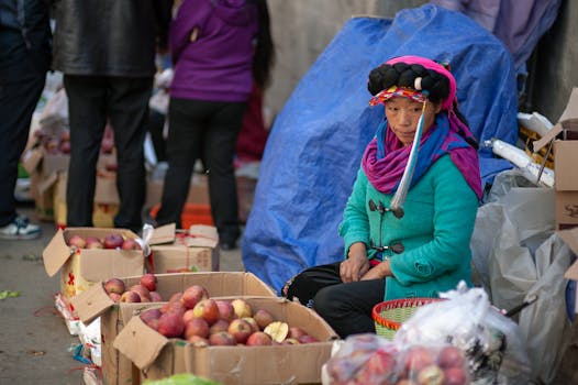 Woman in traditional attire selling apples at outdoor market.