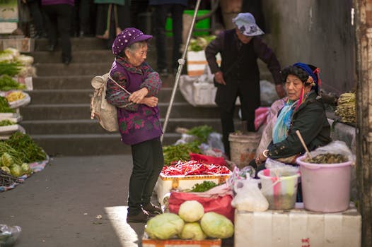 Senior women engaging in conversation at a lively outdoor vegetable market.