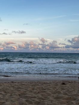 Serene ocean waves with a sandy beach and pink clouds at sunset.