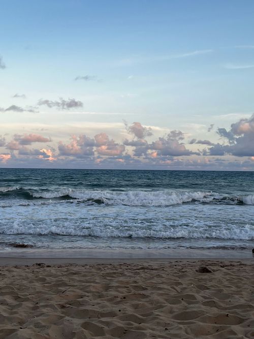 Free Serene ocean waves with a sandy beach and pink clouds at sunset. Stock Photo