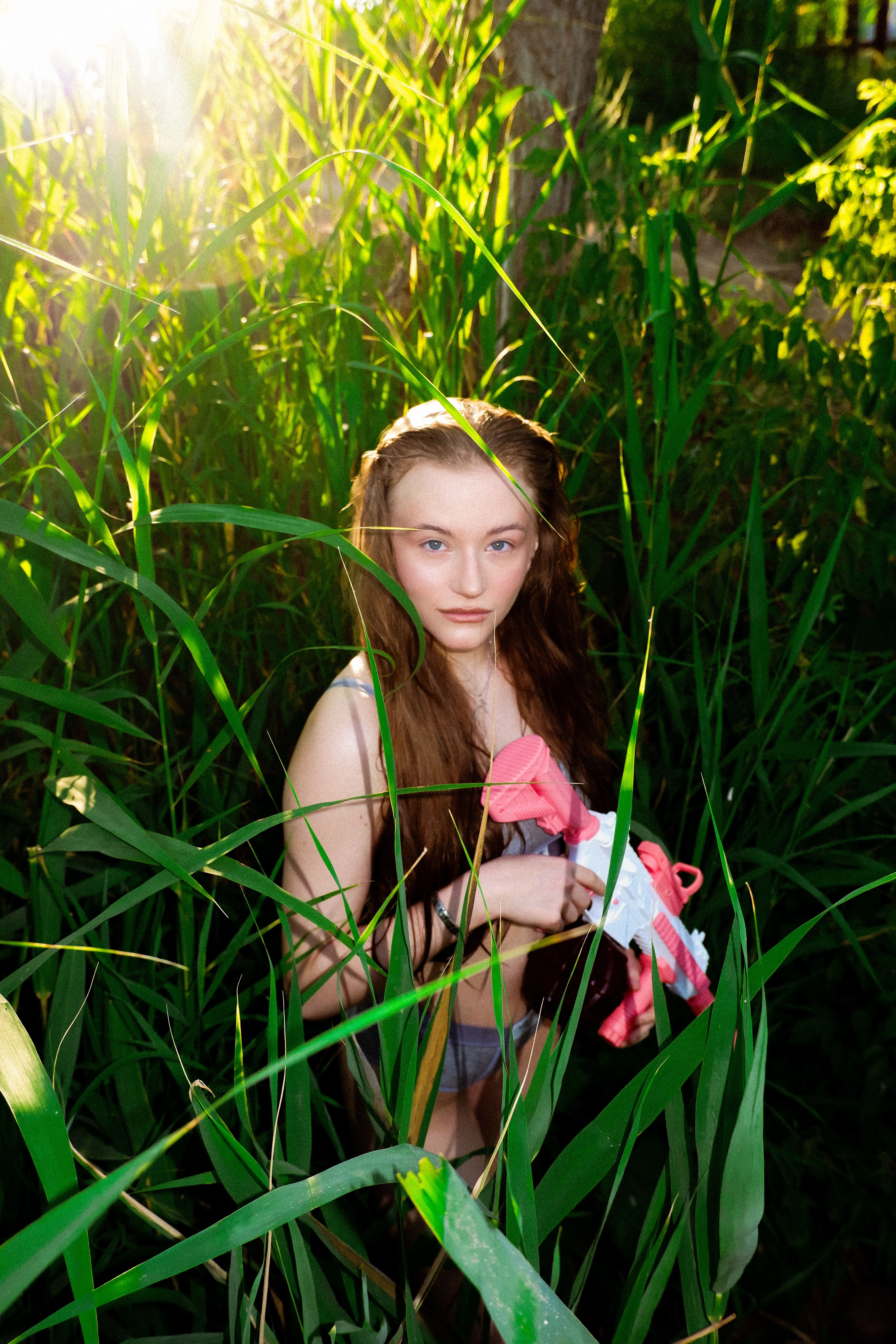 A young woman stands amidst tall grass holding a colorful toy gun.