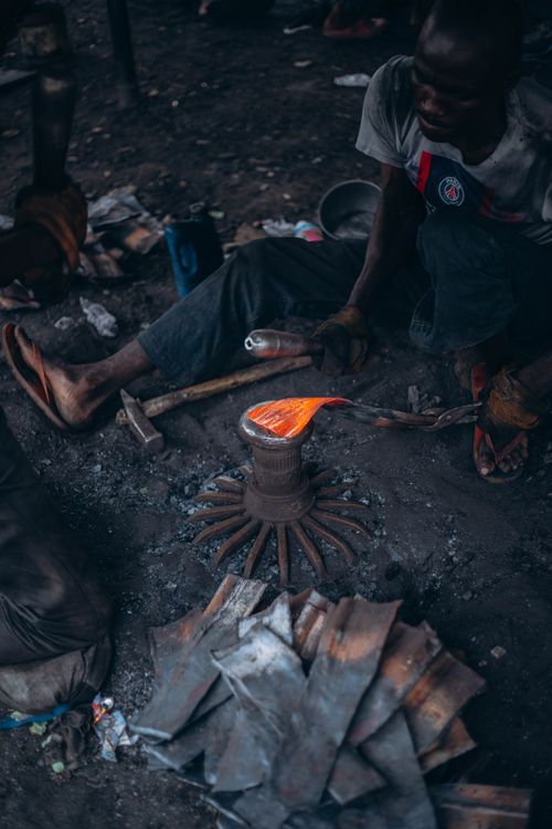 Free A blacksmith skillfully shapes hot metal over a fire outdoors. Stock Photo