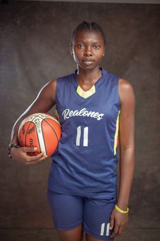 Confident female basketball player posing with basketball in uniform.
