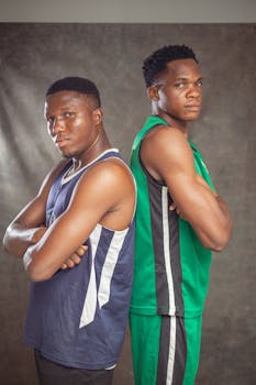 Two young athletes in basketball jerseys stand back-to-back, exuding confidence.