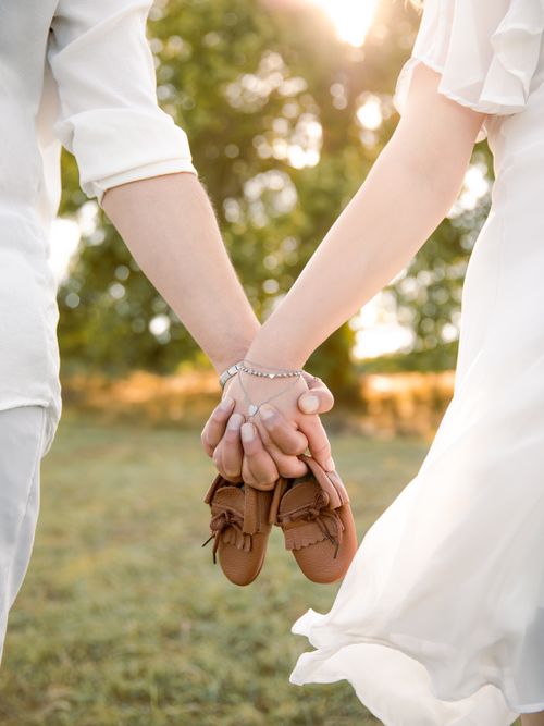 Free Couple holding baby shoes symbolizing new beginnings in a sunlit field. Stock Photo