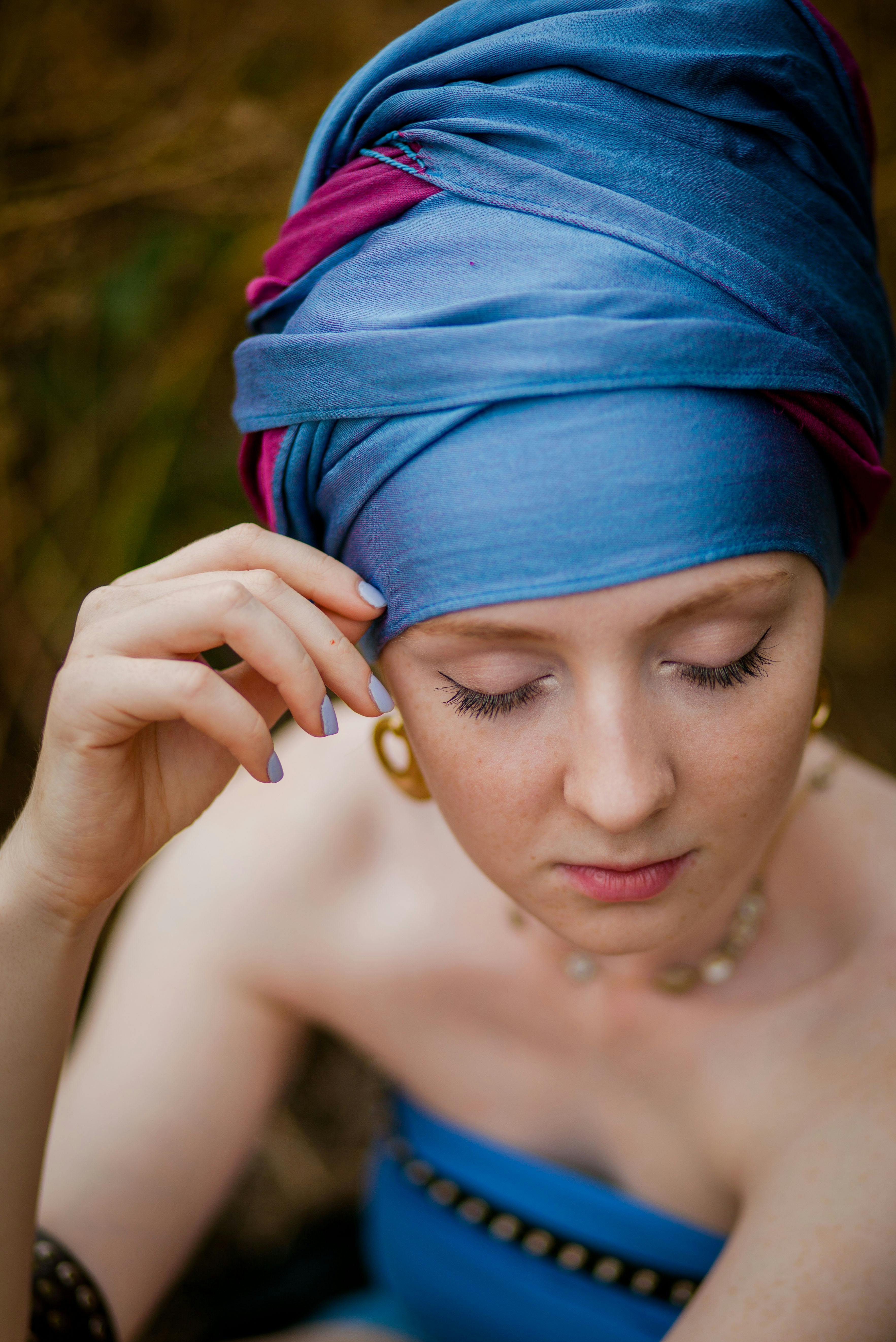Portrait of a woman with blue turban, eyes closed, captured in a serene, natural setting.