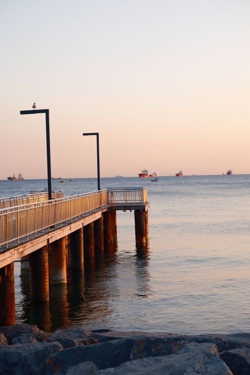 Free A tranquil coastal pier at sunset with ships in the distance, creating a peaceful seascape. Stock Photo
