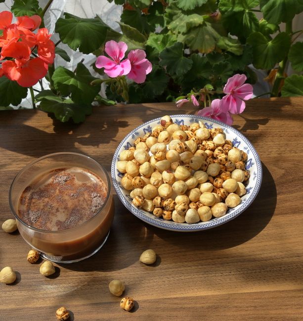 A small bowl of toasted, skinned hazelnuts next to a few in their brown papery skins, showing the color difference after roasting.