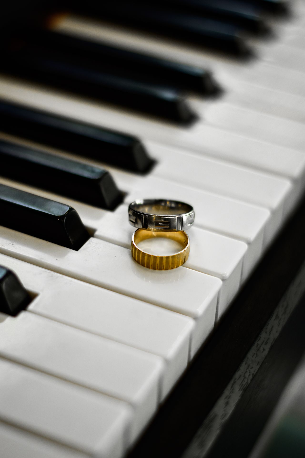 Two plain wedding bands, one brushed silver and one ribbed gold, resting together on the white keys of a piano