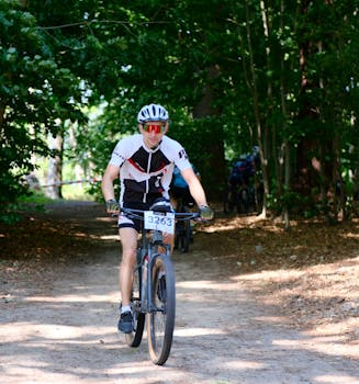 A cyclist participates in a mountain bike race through a sunlit forest trail.