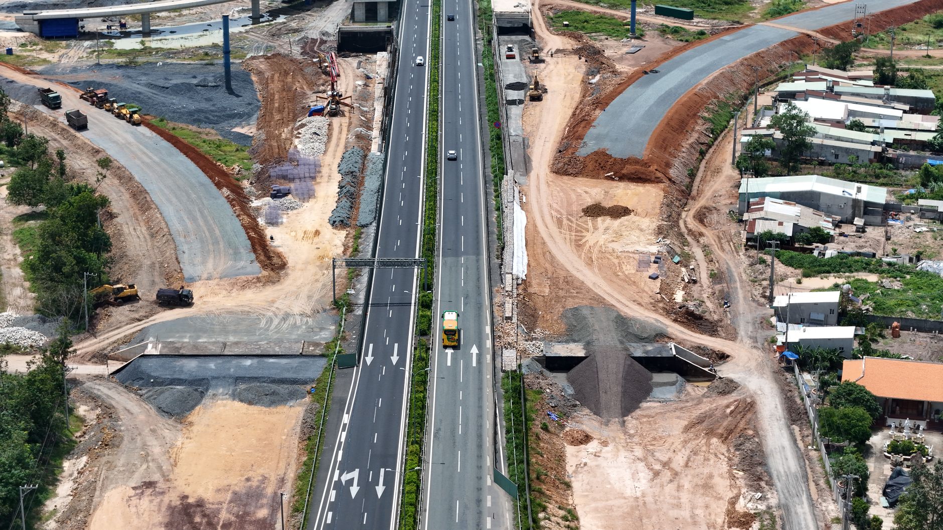 Aerial shot of highway construction with vehicles and residential area, Vietnam.