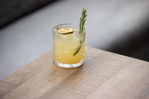 Free A citrus cocktail garnished with a dried citrus slice and rosemary on a wooden table. Stock Photo
