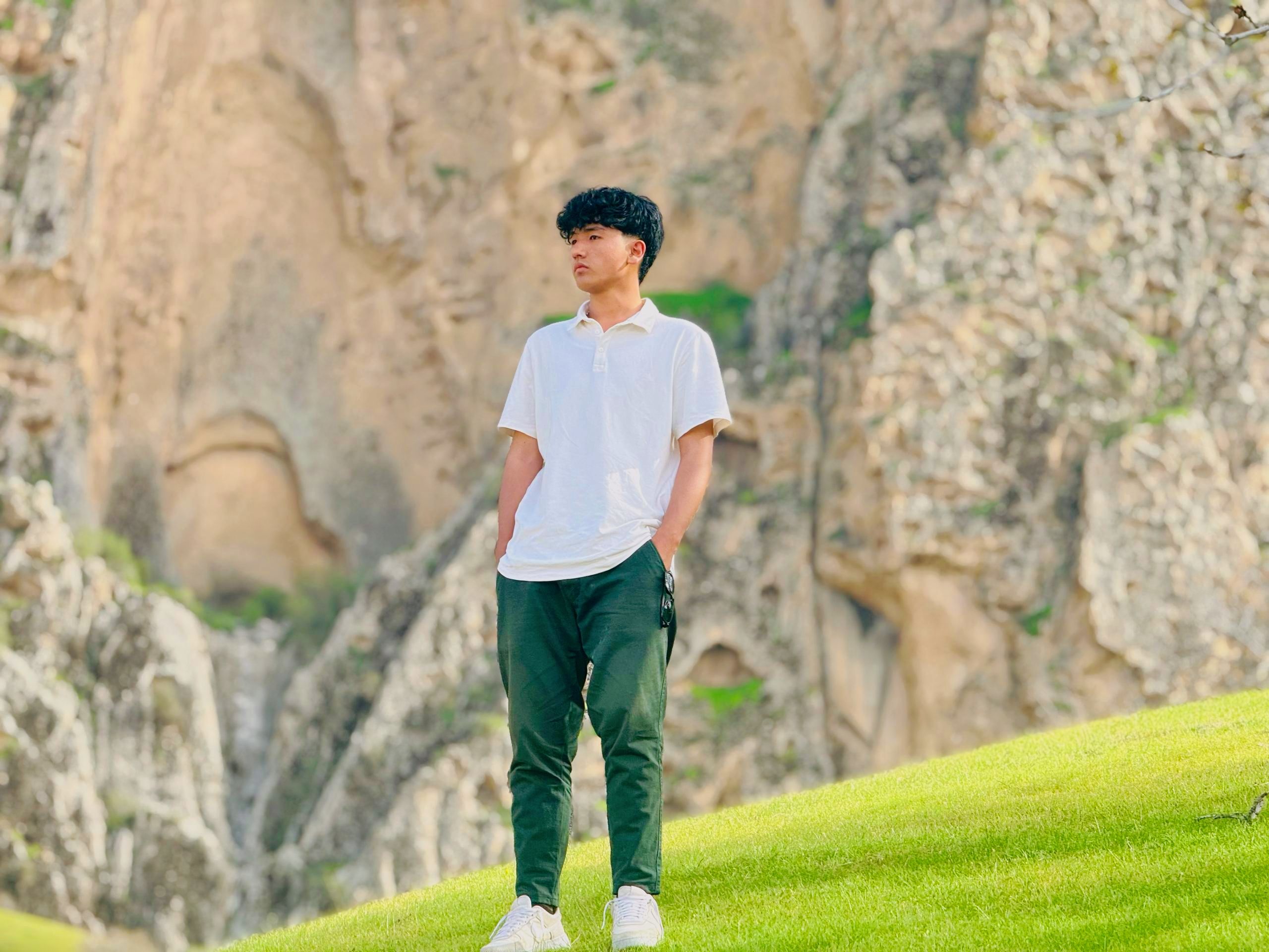 Young Man in White Shirt Standing by Rocky Cliff
