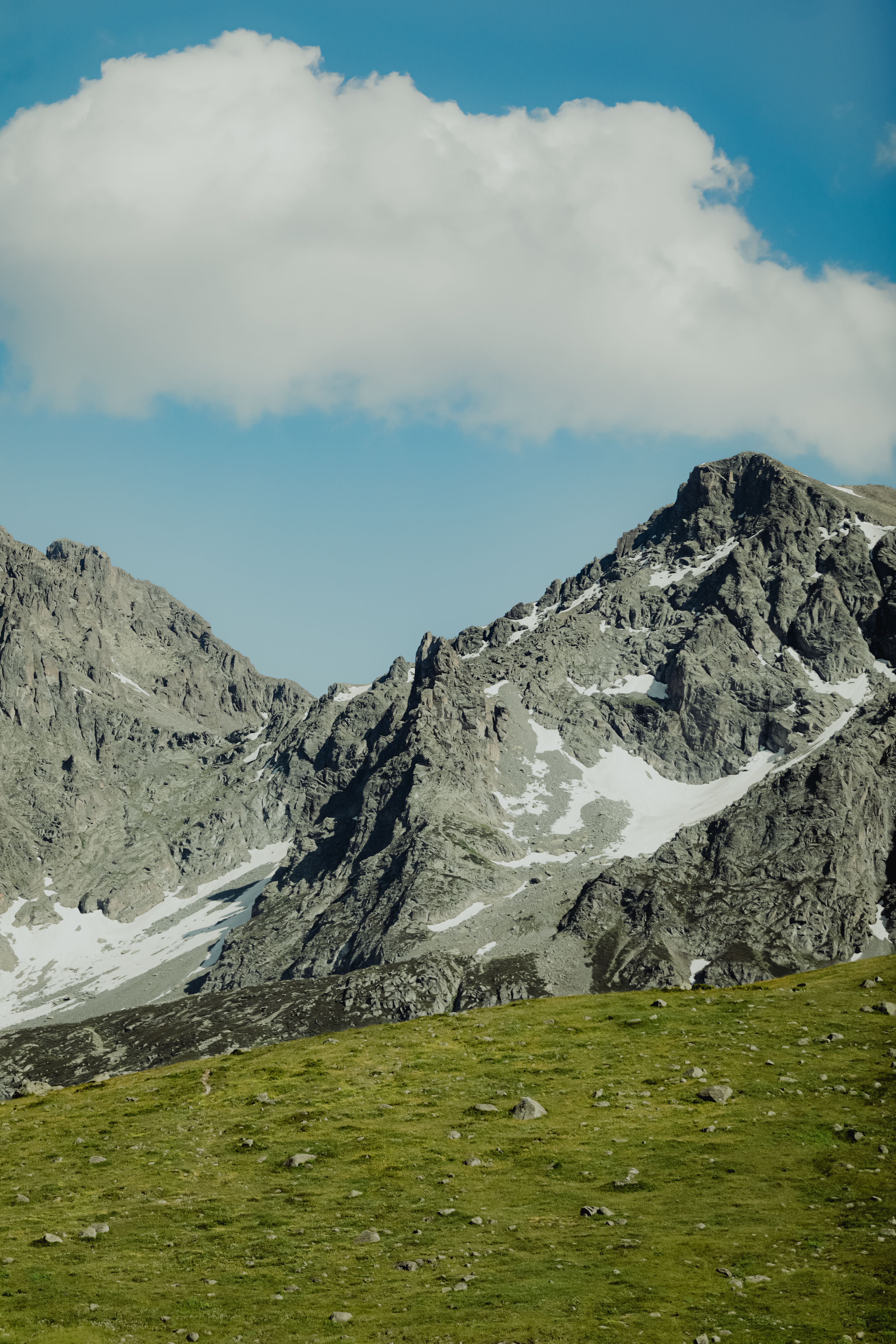 A breathtaking view of rugged mountains with snow patches under a cloudy blue sky.