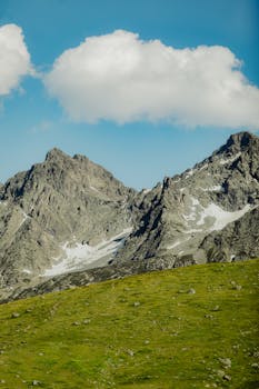 Picturesque mountains with snow patches under blue sky and fluffy clouds.