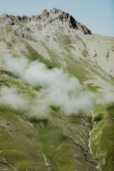 Dramatic mountain peaks with lush greenery and drifting clouds in a serene outdoor setting.