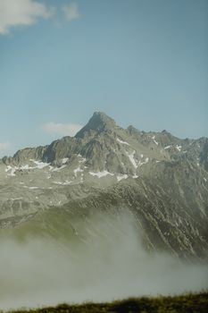 Stunning mountain peak surrounded by mist and clear blue sky, capturing nature's tranquility.