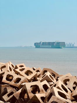 Large cargo ship passing by geometric blocks at Tianjin port, under clear blue skies.
