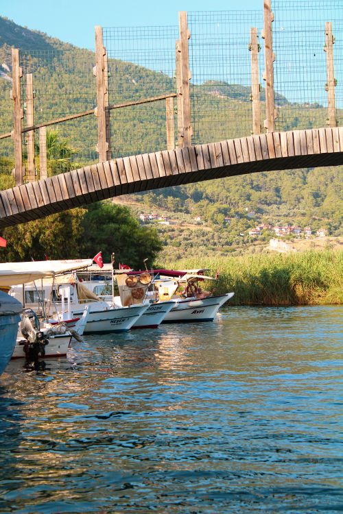 Free Wooden boats docked under a scenic bridge in Akyaka, Muğla, Türkiye, surrounded by lush greenery. Stock Photo